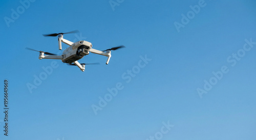 Aerial view of a modern white quadcopter drone with camera flying in clear blue sky during daytime, professional UAV for aerial photography and videography