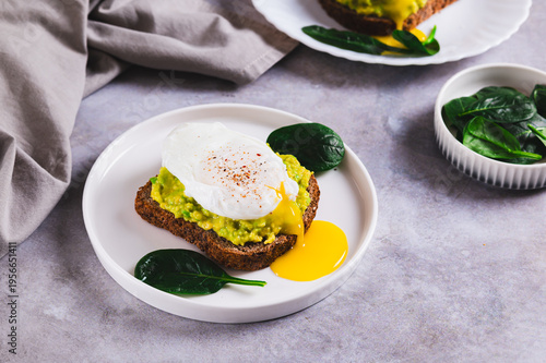 Avocado sandwich with poached egg and spinach on a plate on the table