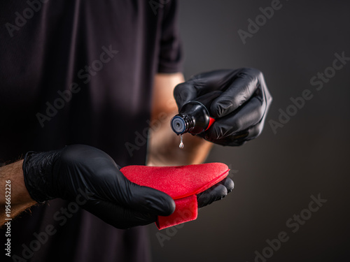 Gloved hands applying ceramic coating liquid onto red sponge for detailing, car ceramics liquid dropping