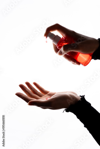 Human hand pressing pump bottle with red lubricant gel onto open palm against white background, backlight highlighting fluid drop and transparency.