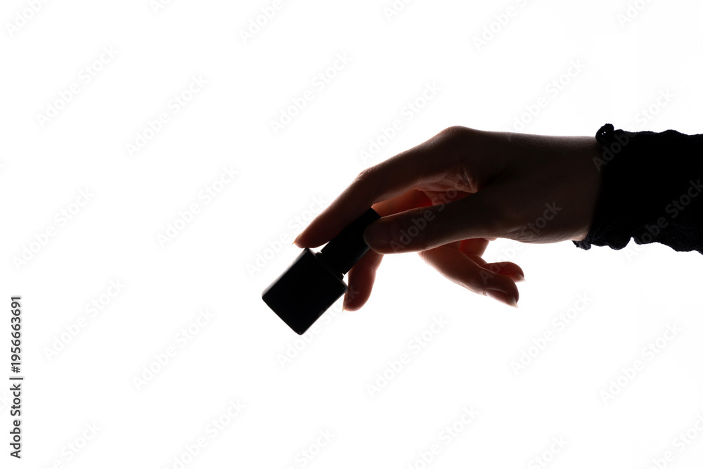 Fototapeta premium Human hand holding nail polish bottle against white background, backlight emphasizing silhouette, shape, and applicator cap.