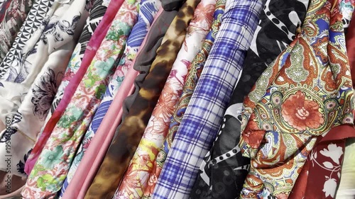 camera moving along colorful cotton and silk fabrics displayed outside shop in windy weather