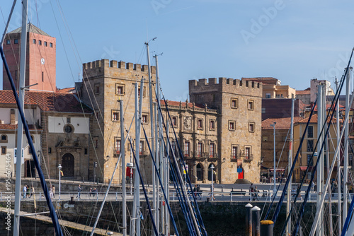 The historic 18th-century Palace of Revillagigedo in Gijon, Spain, seen behind the masts of sailboats at the marina on a bright sunny day. (146 characters)
