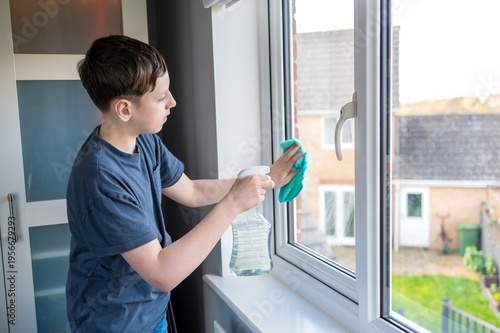 Tableau sur toile Teen boy cleaning window with cloth at home, helping with chores, responsibility learning, everyday routine
