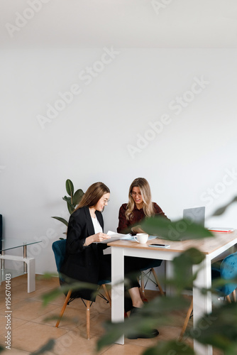 Two women checking paperwork and discussing financial results in modern office.