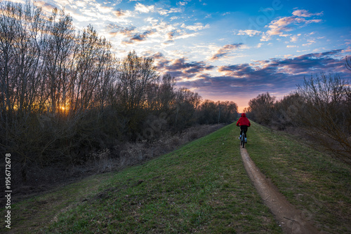 Cyclist on grassy levee near Warsaw rides toward sunrise or sunset