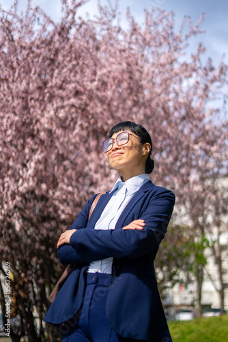 Confident businesswoman with arms crossed in front of blooming cherry blossom tree