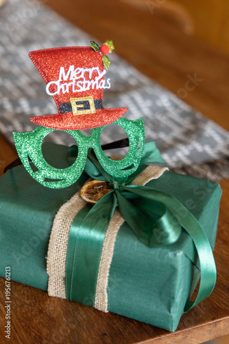 Wrapped gift sitting on wooden table at home wearing green glitter glasses and red top hat