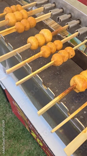 Row automatically rotating meatballs on nine skewers roasting above charcoal barbecue, Thai traditional street food, vertical footage