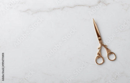 A pair of ornate, vintage-style gold scissors with intricate handle designs rests elegantly on a polished white Carrara marble surface with subtle grey veining, ready for use or display