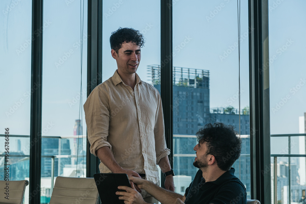 Fototapeta premium Two business colleagues having an informal conversation, collaborating on a project in a modern office with city views