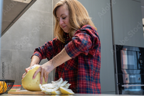 Billede på lærred Woman peeling pomelo on countertop in modern kitchen wearing red plaid shirt rem