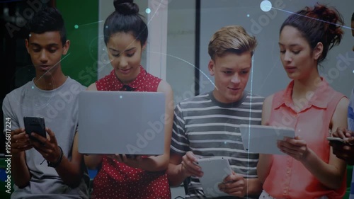 Rightmost lifting tablet starting classmates leaning in and sharing screens to compare content