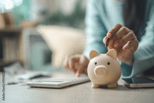 Bilde på lerret Person putting coin into piggy bank next to calculator and smartphone representing personal finance planning, saving money, budgeting and financial goals