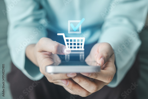 Photos Customer confirming a successful online purchase on smartphone with digital shopping cart and check mark icon