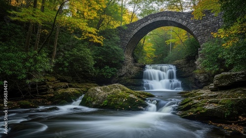 A serene waterfall flows under a historic stone bridge in a lush forest
