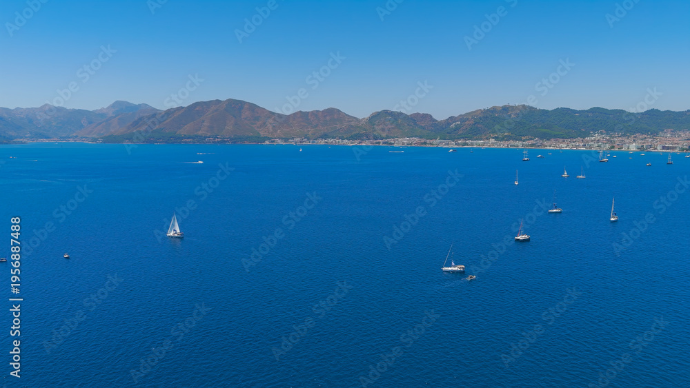 Obraz premium Marmaris, Turkey. Low aerial panoramic view of Marmaris Bay filled with yachts. The city and shoreline are visible in the distance on a bright summer day.. Aerial View