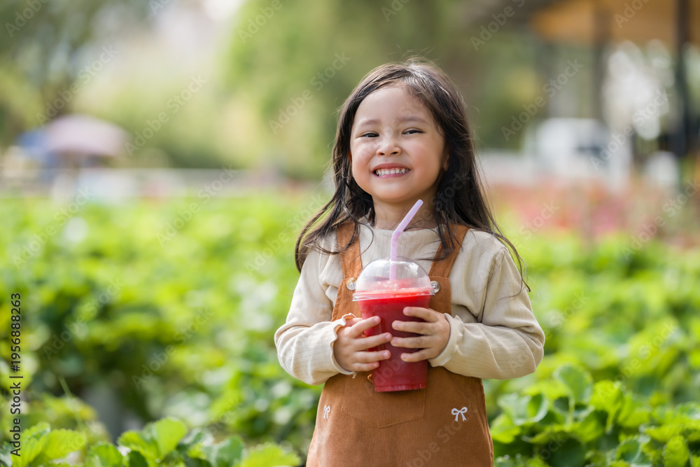 Fototapeta premium happy preschool child girl holding a cup of fresh strawberry smoothie in farm
