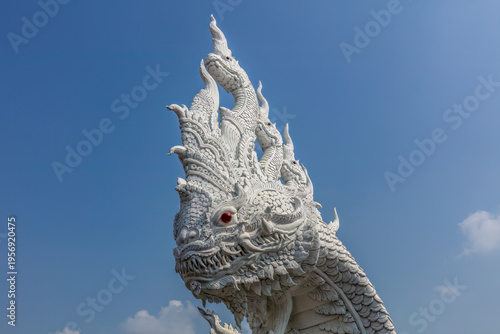 Closeup of white statue depicting a naga serpent, at the buddhist temple of Wat Don Yai, northeast of Bangkok, Thailand. Blue sky in background.