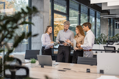 Group of business people standing together and discussing their work and projects, having a team meeting in an office.
