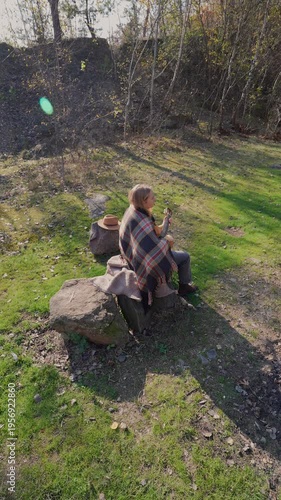 Blonde woman playing string guitar outdoors in autumn forest. Concept of sound therapy, mental health and wellness rituals. Calmness tranquility audio-sensory practices. Aura farming energy holistic