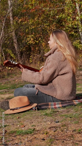 Portrait of smiling caucasian artist plays wooden acoustic guitar in autumnal park. Young songwriter plays string musical instrument hobby outside in nature fall time. Audio music healing in natural