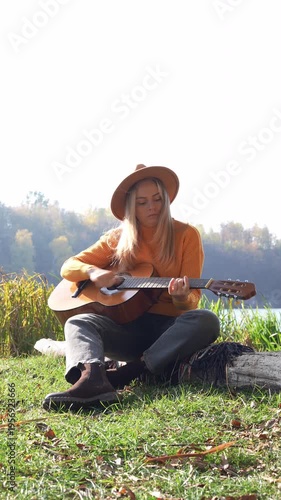 Portrait of smiling caucasian artist plays wooden acoustic guitar in autumnal park. Young songwriter plays string musical instrument hobby outside in nature fall time. Audio music healing in natural