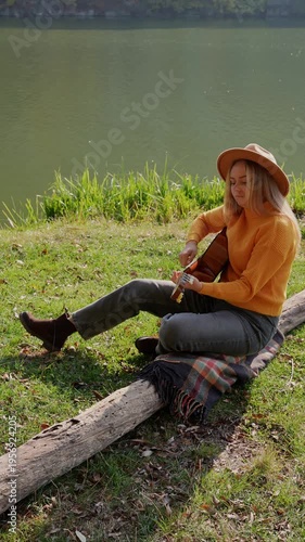 Blonde woman playing string guitar outdoors in autumn forest. Concept of sound therapy, mental health and wellness rituals. Calmness tranquility audio-sensory practices. Aura farming energy holistic