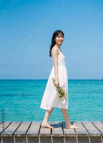 Authentic young woman walks holding wildflowers on a sunny wooden pier coast view