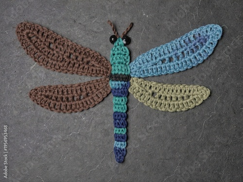 Crocheted Dragonfly Applique Craft Project with Brown Blue Green Wings on Dark Stone Surface