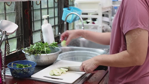 Close up of woman hands using a knife to slice fresh green eggplant on a white cutting board. Housewife preparing healthy vegetables for cooking a meal in the home kitchen.