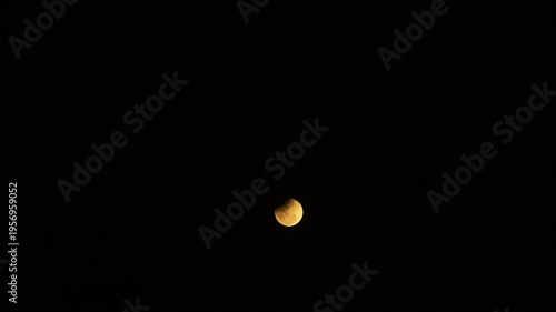 4K Timelapse video of a total lunar eclipse ending phase. The glowing moon slowly emerges from the Earth's shadow in the dark night sky with moving clouds passing by.