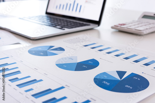Close up of financial document with pie charts and bar graphs on office desk with laptop and calculator