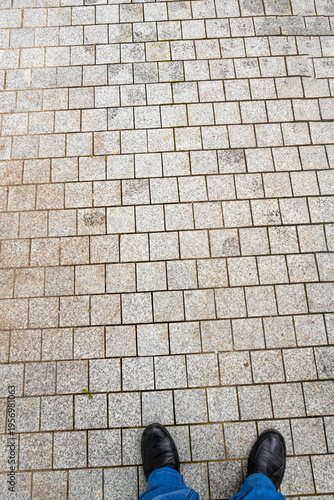 Person standing on a paved pathway with gray stones during daylight in an urban area