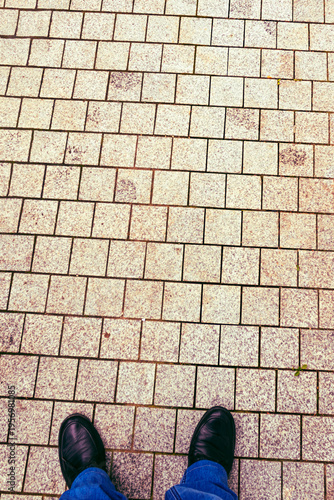 Person standing on a paved pathway with gray stones during daylight in an urban area
