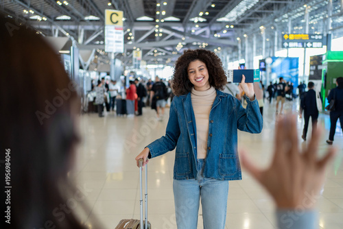 Latina woman happily waving to greet her friend in the airport terminal. 
