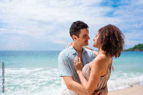 Caucasian young man hugging his Latina girlfriend on a sandy beach. 