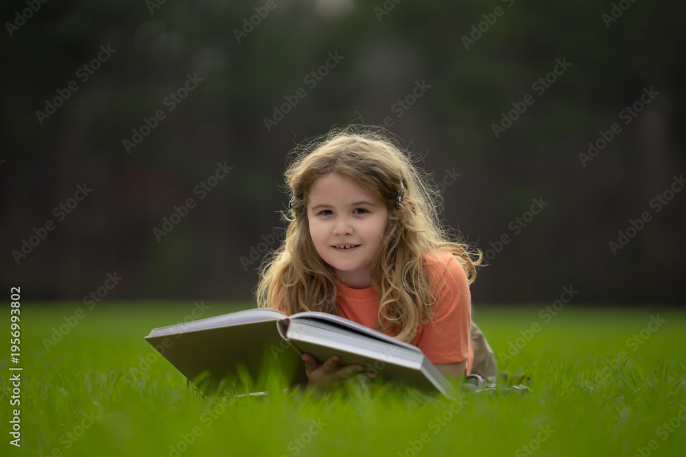 Obraz premium Kid read a book in the grass. Kid read a book story outdoors. Kid read book in the meadow on a sunny day. Reading in nature. Schoolboy with book. Kid outdoor learning. Kids read story.