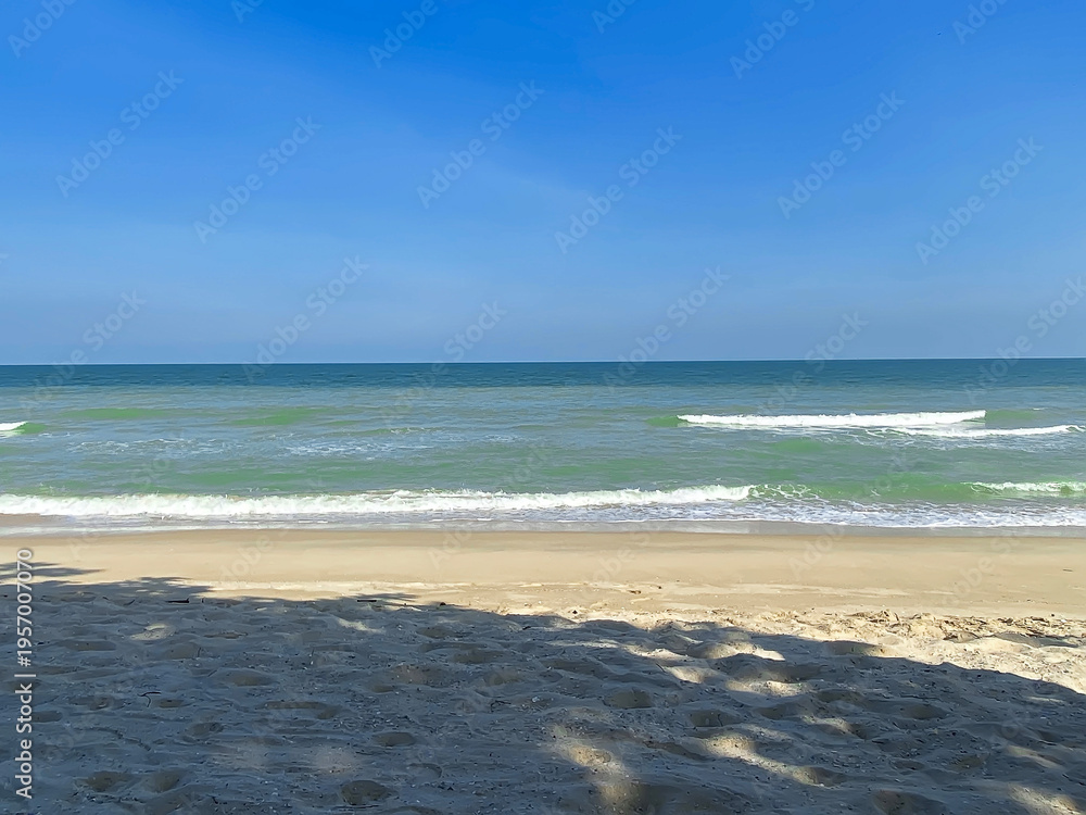 Fototapeta premium Tranquil beach with gentle waves, clear sky, and soft sand in bright sunlight.