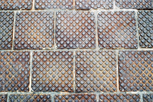 Rusted metal tiles with a diamond pattern. The surface is weathered, showing a mix of blue and orange tones highlighting the intricate design.