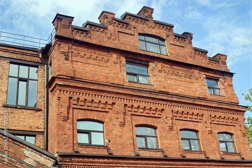 Classic multi-story brick building showcases intricate architectural details, large windows, and a steep roof against a clear blue sky.