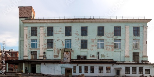Weathered building shows peeling paint and exposed brickwork, evoking a sense of urban decay and history under a clear sky.