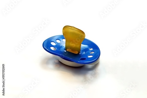 Blue baby pacifier with a yellow nipple sits on a white surface, featuring multiple ventilation holes for safety.