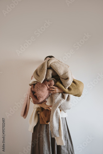 Close Up Of Hands Carrying A Stack Of Warm Woolen Jumpers Against White Wall