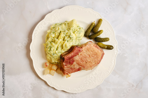 Tableau sur toile Enjoying a pork rib chop meal with mashed potatoes and pickles on a white plate