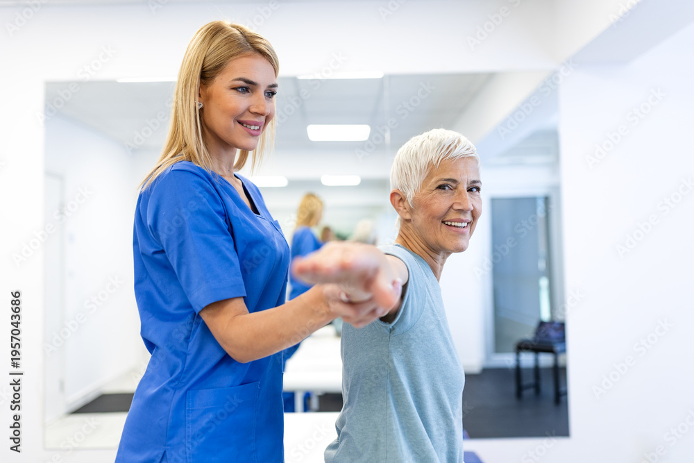 Fototapeta premium Senior woman performing arm stretching exercises with a physiotherapist. Physical therapy for shoulder mobility in a modern clinic. Healthcare and medicine concept. Elderly patient rehabilitation.