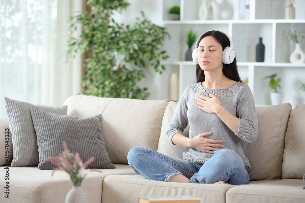 Obraz premium Asian woman doing online guided breathing exercise on a couch