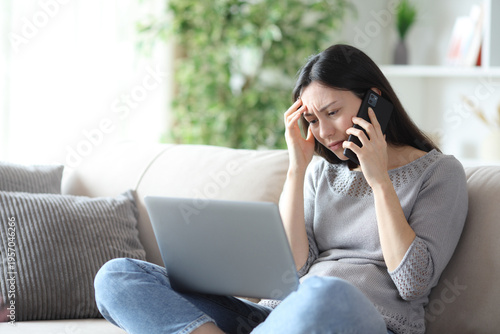 Canvas Print Worried asian woman checking laptop and talking on phone