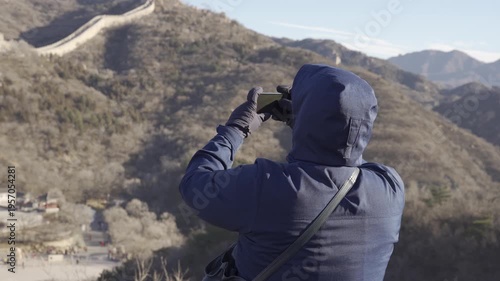 an asian man while take photo with smartphone mobile phone while traveling on the great wall of China in winter day,man travel at the great wall of china on mountain hill