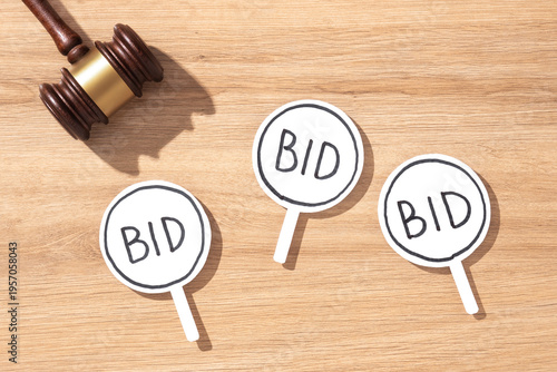 Foto Wooden gavel next to multiple white BID signs on a wooden desk, symbolizing auction bidding and competitive sales